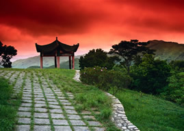 A pagoda at the end of a stone path againt a red sky